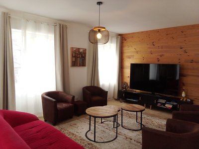 Grand séjour lumineux avec canapé, fauteuil et écran plat.
