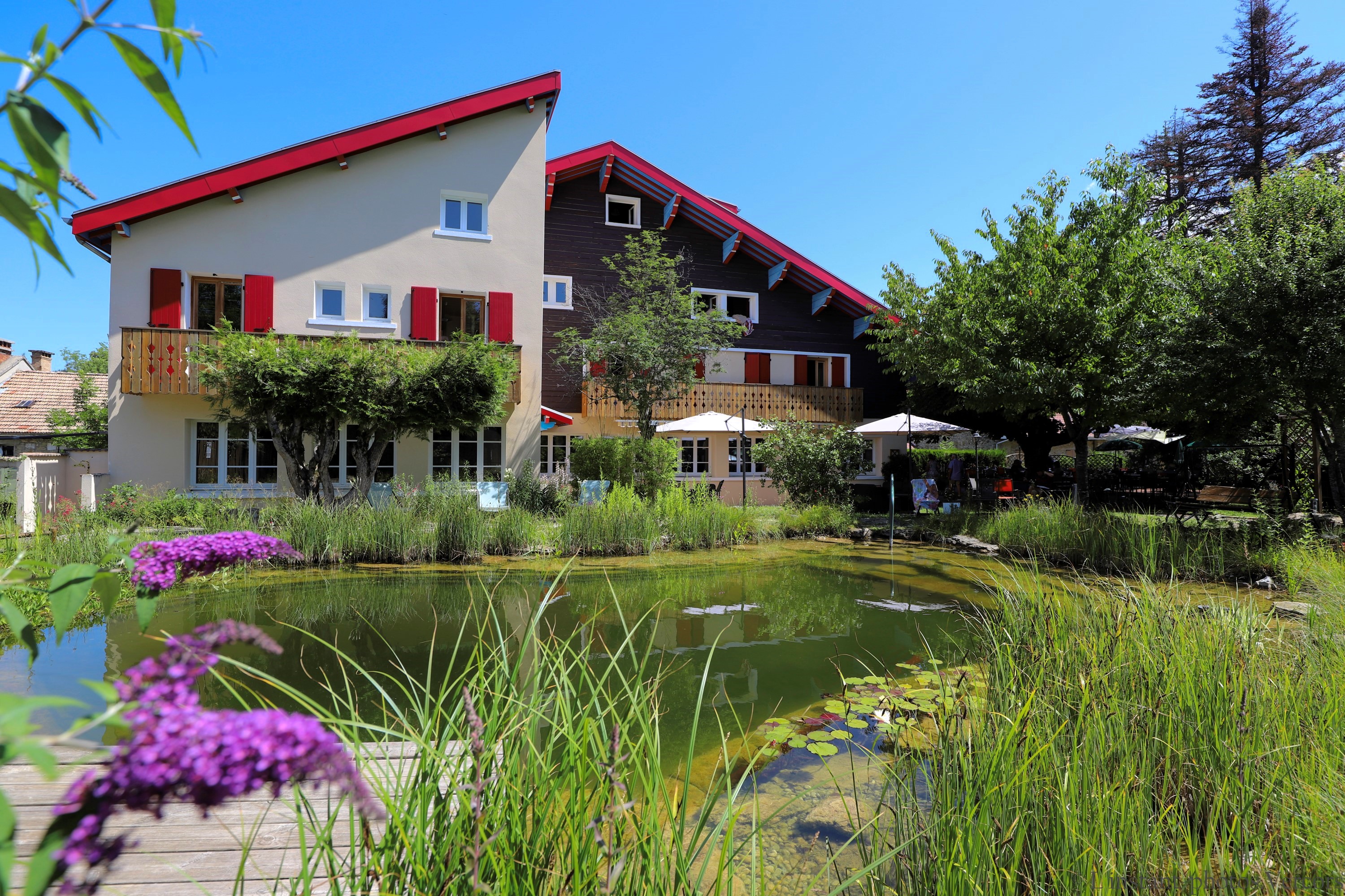Vue extérieure de l’établissement regroupant l’hôtel et le restaurant avec une mare naturelle au premier plan